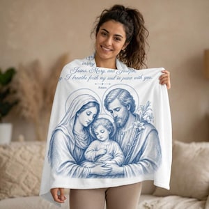 May include: A white blanket featuring a blue illustration of Jesus, Mary, and Joseph, with the text "Jesus, Mary, and Joseph, I breathe forth my soul in peace with you. Amen." The blanket has a religious theme.