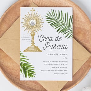 Könnte beinhalten: Eine weiße Einladungskarte mit goldenen religiösen Bildern und grünen Palmfarnen, auf einem Holztablett mit einem braunen Umschlag. Der Text auf Spanisch enthält "Cena de Pascua" und Veranstaltungsdetails.