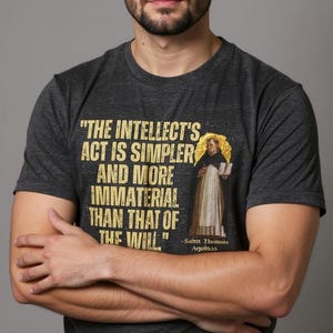 Könnte beinhalten: Dunkelgraues T-Shirt mit dem Zitat "THE INTELLECT'S ACT IS SIMPLER AND MORE IMMATERIAL THAN THAT OF THE WILL" und einem Porträt einer religiösen Figur. Das Zitat wird Sahn Thonus Aquinas zugeschrieben.