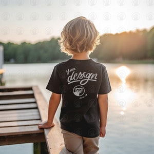May include: A young person wearing a black t-shirt with the text "Your design here" on the back. The person is standing on a wooden jetty overlooking a lake.