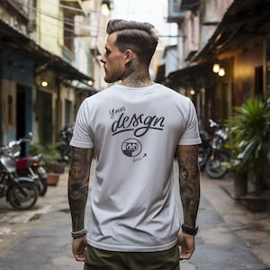 Puede incluir: Una camiseta blanca con un diseño gráfico negro en la espalda. El diseño incluye el texto "Your design here" y una pequeña ilustración de un animal.