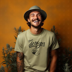 Puede incluir: Un hombre con un sombrero verde y una camiseta verde claro con el texto "Your design here" y un pequeño gráfico de un animal. Está sonriendo y mirando a la cámara.
