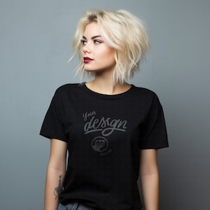 Puede incluir: Una camiseta negra de manga corta y cuello redondo. La camiseta tiene el texto "Your design" impreso en la parte delantera en una fuente estilizada. Un pequeño gráfico de un oso panda está debajo del texto.