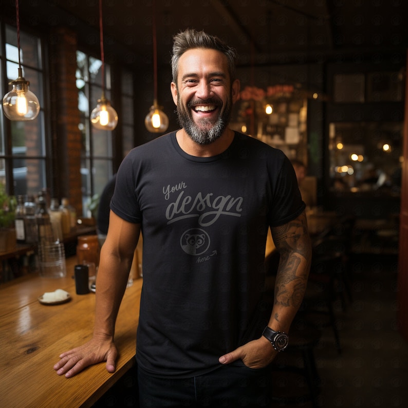 May include: A man wearing a black t-shirt with the text "Your design here" printed on the front. He is standing in a bar setting with a wooden counter in front of him.
