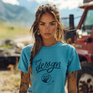 May include: A woman wearing a light blue t-shirt with the text "Your design here" and a small animal graphic. She has long brown hair and is wearing gold earrings.