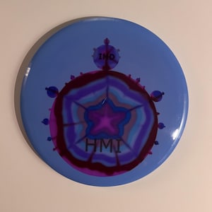 May include: A blue circular disc with a purple and blue abstract design in the center. The design features a five-pointed star and the words "HMI" and "INQ" in black.