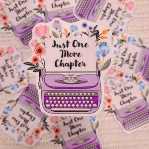 Pode incluir: Adesivo de máquina de escrever roxo com detalhes florais e o texto "Just One More Chapter".