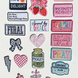 Może przedstawiać: Kolekcja haftowanych naszywek w różnych kształtach i kolorach. Naszywki zawierają frazy takie jak "I'm a Delight", "Saved by Grace" i "Pretty girls hit curbs". Inne wzory to truskawka, słoik ogórków i błyskawica.