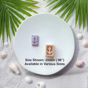 May include: Two rectangular anchor-themed objects, one lavender and one tan, are displayed on a white plate. The text "Size Shown: 25mm (.98") Available in Various Sizes" is below the objects. The background includes shells and palm leaves.