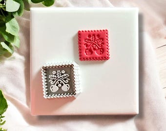Pode incluir: Dois cortadores de biscoitos de plástico branco com um design em relevo de um ramo de cerejeira com folhas e cerejas. O cortador à esquerda está sobre uma superfície branca. O cortador à direita é vermelho.