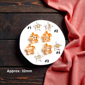 May include: A collection of turtle-shaped decorative items, each approximately 1.25 inches in size, with various designs including flowers, pineapples, and seashells. The items are arranged on a white plate, with the text "Approx: 32mm" visible.