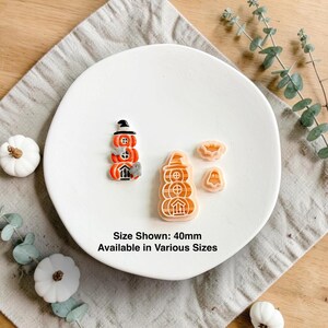 Op de afbeelding: Een set van drie Halloween-koekjesvormpjes, waaronder een gestapeld pompoenhuis, een vleermuis en een spookje. De tekst luidt: Size Shown: 40mm Available in Various Sizes.