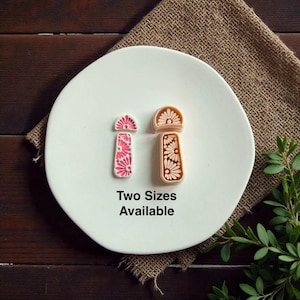 May include: Two floral design stamps, one pink and one tan, are displayed on a white plate. The pink stamp has a pink and white floral pattern. The tan stamp has a tan and white floral pattern. The text "Two Sizes Available" is below the stamps.