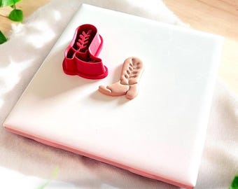 Könnte beinhalten: Zwei rote und braune Cowboy-Stiefel-Ausstecher aus Plastik auf einer weißen Oberfläche.