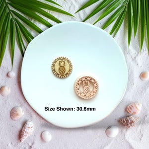 May include: Two wooden pineapple-themed stamps, one with a solid design and the other with a cut-out design, are displayed on a white plate. The size shown is 30.6mm. The background includes seashells and palm leaves.