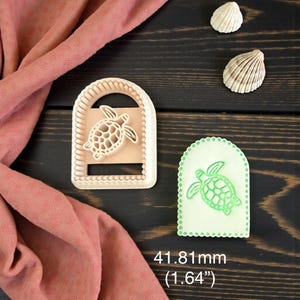 May include: A light-colored cookie cutter with a turtle design, next to a green cookie with the same design. The cutter is 1.64 inches in height. Two seashells are also in the image.