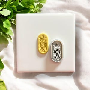 May include: Two pineapple shaped cookie cutters, one yellow and one gray. The yellow cutter is solid and the gray cutter is open.