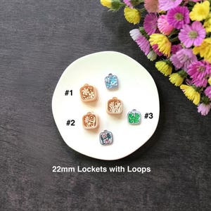 May include: A collection of square 22mm lockets with loops, each featuring a unique floral design. The lockets are displayed on a white plate, with a variety of colors and patterns. The image includes text that reads "22mm Lockets with Loops."