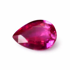 Può includere: Una gemma di rubino sfaccettata a forma di pera. La gemma è di un colore rosa intenso e vibrante con un alto grado di purezza. Il taglio della pietra permette alla luce di riflettersi, creando una brillantezza scintillante. Il rubino è su uno sfondo bianco.