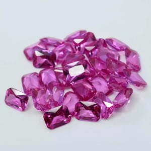 May include: A pile of pink, faceted gemstones. The gemstones are cut in a rectangular shape with pointed edges.