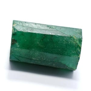 May include: A large, deep green emerald crystal with a faceted, rectangular shape. The crystal has a smooth, polished surface and is translucent.