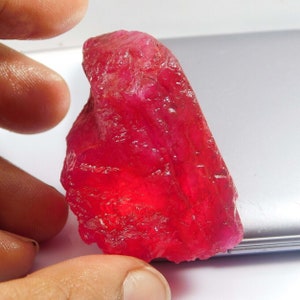 May include: A large, rough, red ruby gemstone. The ruby is a deep red color and has a natural, unpolished finish.