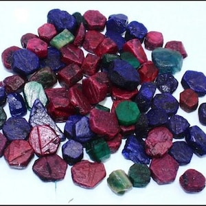 Op de afbeelding: Een verzameling losse edelstenen in verschillende tinten rood, blauw en groen. De edelstenen zijn gefacetteerd en hebben een gepolijste afwerking.
