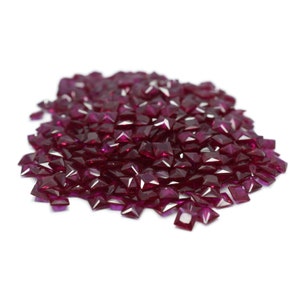 May include: A pile of loose, faceted ruby red gemstones. The stones are square shaped and have a polished finish.
