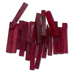 Pode incluir: Uma coleção de pedras preciosas retangulares, vermelho escuro, de tamanhos e formas variadas, está espalhada sobre um fundo branco. As pedras têm uma aparência polida, com texturas de superfície e variações de cor visíveis, sugerindo formações naturais.