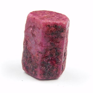 Può includere: Un cristallo di rubino rosa intenso con forma esagonale e una superficie ruvida e testurizzata.