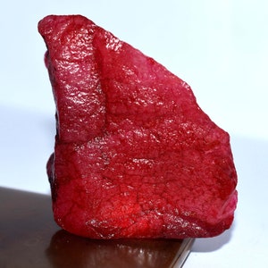 Pode incluir: Uma grande gema vermelha bruta com uma cor profunda e rica. A gema tem um acabamento natural não polido.