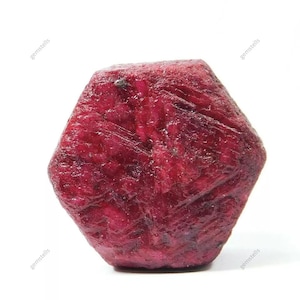 Puede incluir: Una piedra preciosa de rubí rojo intenso con forma hexagonal y una superficie rugosa y natural.
