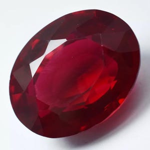 May include: A deep red oval-shaped gemstone with a faceted cut.