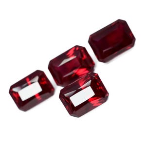 Puede incluir: Cuatro piedras preciosas de color rojo oscuro, talla esmeralda, sobre un fondo blanco.