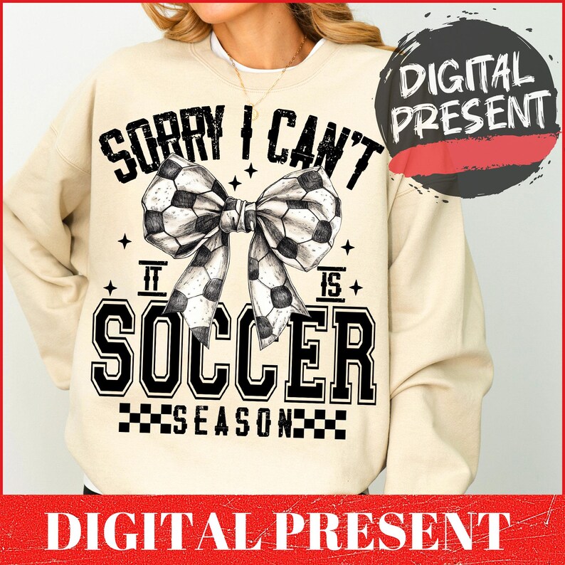 May include: A beige sweatshirt with a black and white graphic design. The graphic features a soccer ball bow with the text "Sorry I Can't It Is Soccer Season".