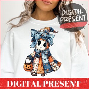 Puede incluir: Sudadera blanca con un diseño de Halloween. El gráfico muestra una figura similar a un espantapájaros con cabeza de calabaza, vestida con un atuendo de retazos y sosteniendo una linterna. El texto "DIGITAL PRESENT" se muestra en una pancarta roja.