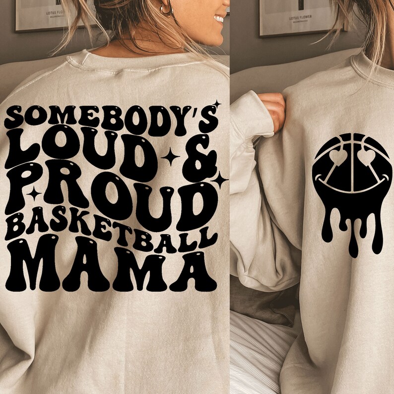 Pu&ograve; includere: Una felpa beige con testo nero che recita "Somebody's Loud & Proud Basketball Mama" e una palla da basket nera con occhi e un sorriso che cola sul retro.