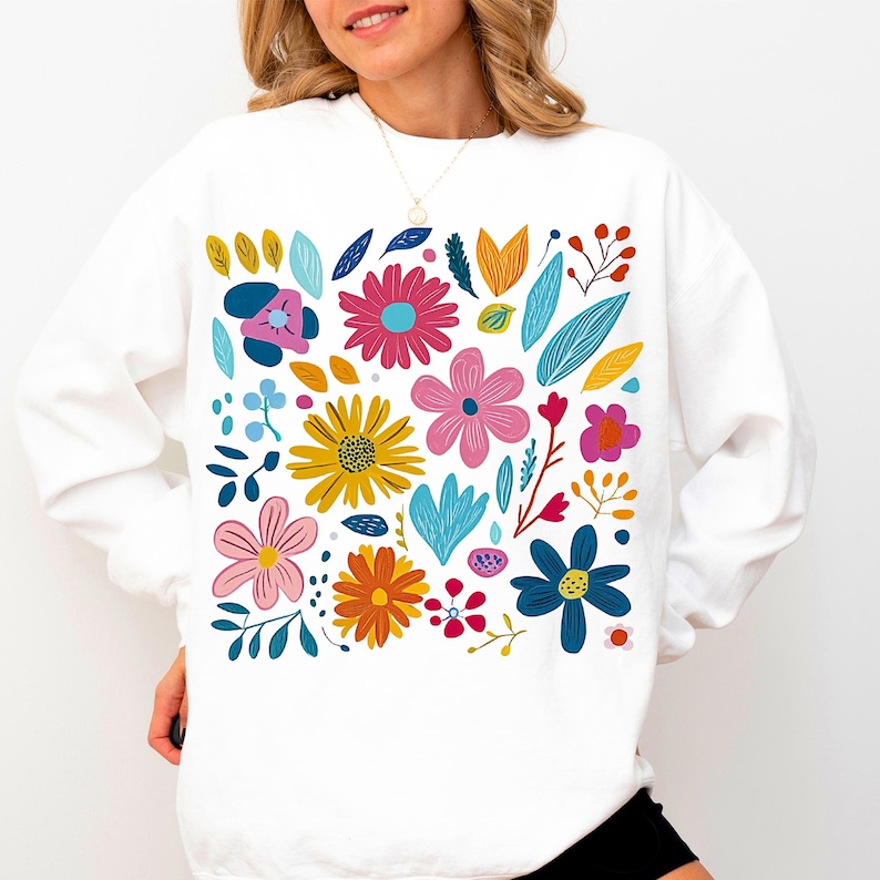 May include: White sweatshirt with a colourful floral print featuring various flowers, leaves, and stems in shades of pink, blue, yellow, orange, and green.