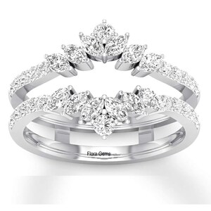 May include: A silver ring with a marquise-shaped diamond setting. The ring is accented with smaller round diamonds. The ring is engraved with the words "Flora Gems".