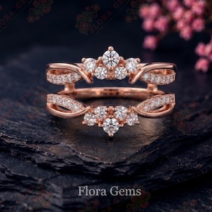 May include: A rose gold ring guard featuring two bands connected by a bridge, adorned with multiple small round white stones. The design includes a crown-like cluster of stones at the top and bottom, with pavé-set stones along the split shanks.