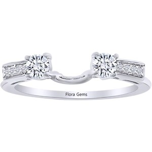 Peut inclure: Une monture de bague en argent avec deux diamants ronds. La monture a un design délicat avec de petits diamants de chaque côté des diamants centraux plus grands. La bague est gravée des mots "Flora Gems".