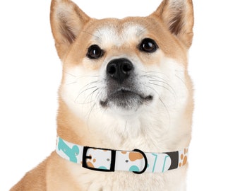 Op de afbeelding: Een Shiba Inu-hond met een patroonhalsband. De halsband is wit met een herhalend patroon van lichtblauwe, bruine en zwarte vormen. De hond heeft bruin en witte vacht en kijkt omhoog.