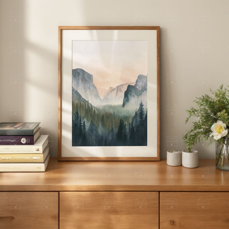 May include: A framed watercolor painting of a mountain range with a forest in the foreground. The mountains are a soft blue and purple, and the forest is a deep green. The sky is a pale pink and orange.