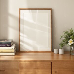 May include: A wooden frame with a white mat and a blank white canvas inside. The frame is sitting on a wooden dresser with a stack of books and two small decorative pots.