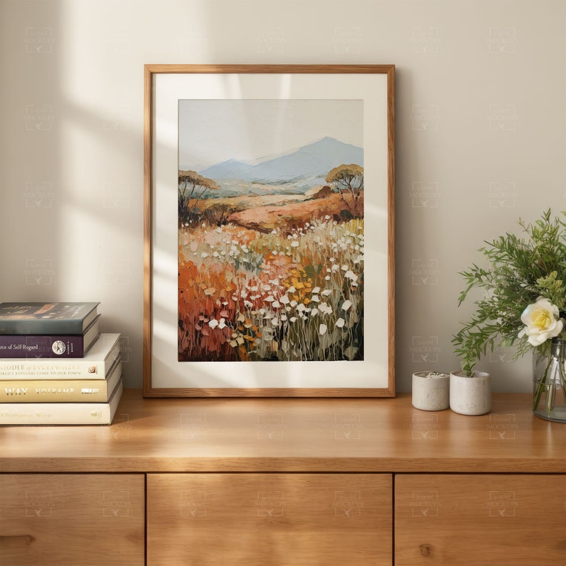 May include: A framed painting of a landscape with a field of white flowers in the foreground and a mountain range in the background. The painting is in a wooden frame and is hanging on a wall.