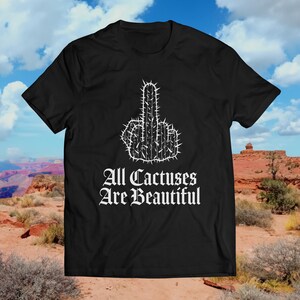 May include: Black t-shirt with a white cactus design shaped like a middle finger. The text "All Cactuses Are Beautiful" is printed below the cactus.