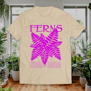 May include: A beige t-shirt with a pink fern illustration and the word "FERNS" in pink lettering. The text below the illustration describes ferns with the scientific classification: Kingdom Plantae, Class Polypodiopsida, Class Filicopsida.
