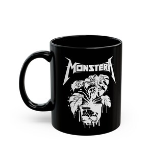May include: Black ceramic coffee mug with a white graphic of a monstera plant in a skull-shaped pot. The text "MONSTERA" is printed in white above the plant.