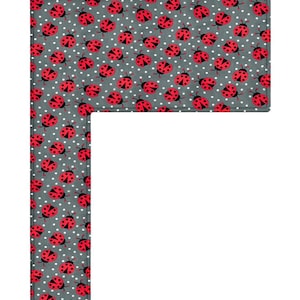 May include: An L-shaped fabric piece featuring a dark grey background with a repeating pattern of small red ladybirds and tiny white polka dots. The edges are finished with a visible stitched border, creating a clean and defined rectangular shape.