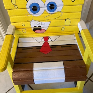 May include: A yellow wooden rocking chair painted to look like Spongebob Squarepants. The chair has a brown seat and a white stripe around the bottom.